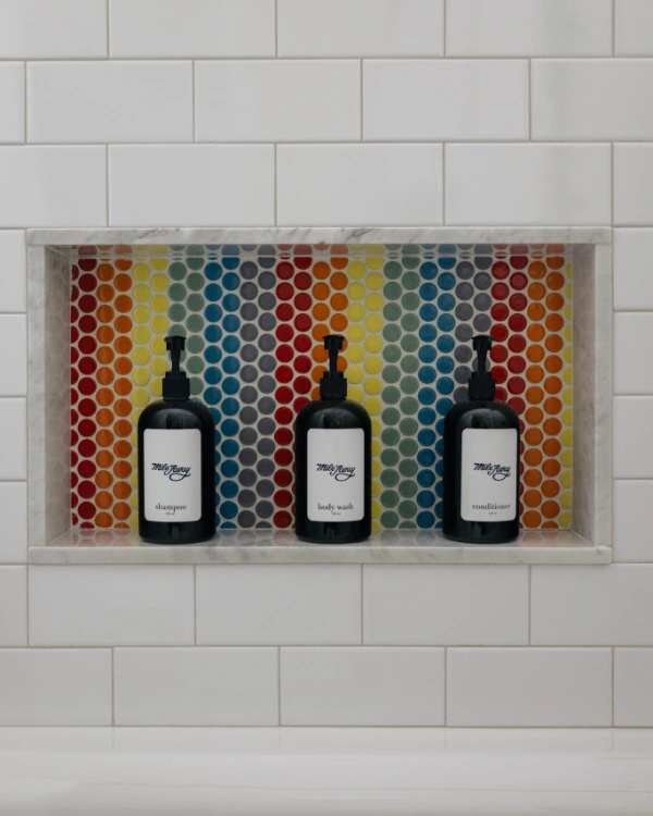 Colorful kids bathroom vanity with rainbow penny tile accent wall, dual faucets, round mirror, and open shelving